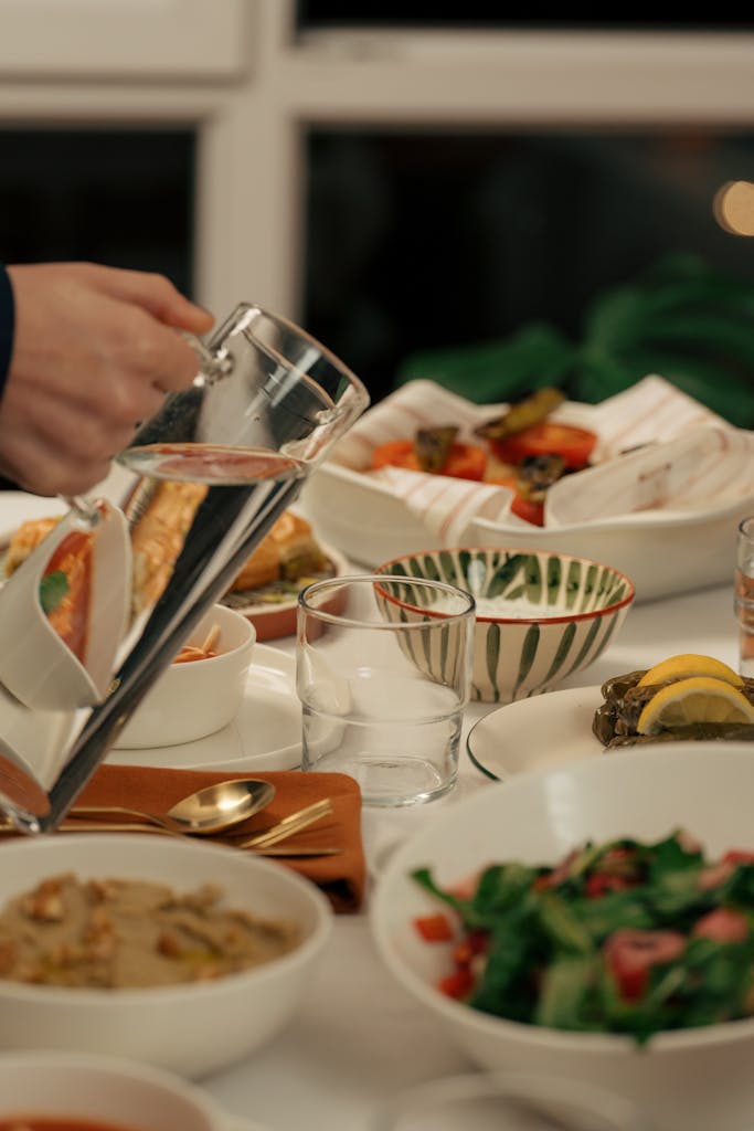 A beautifully set dinner table with various dishes and a hand pouring water into a glass.
