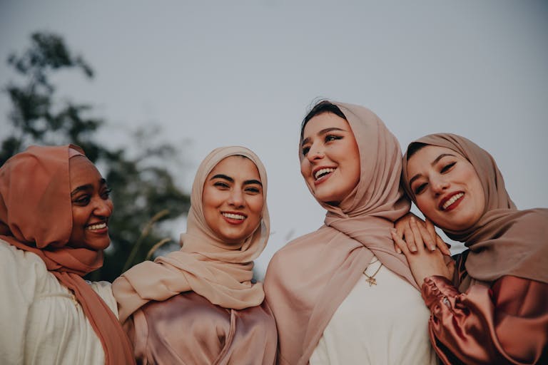 Four diverse women in hijabs laughing together outdoors, embracing friendship.