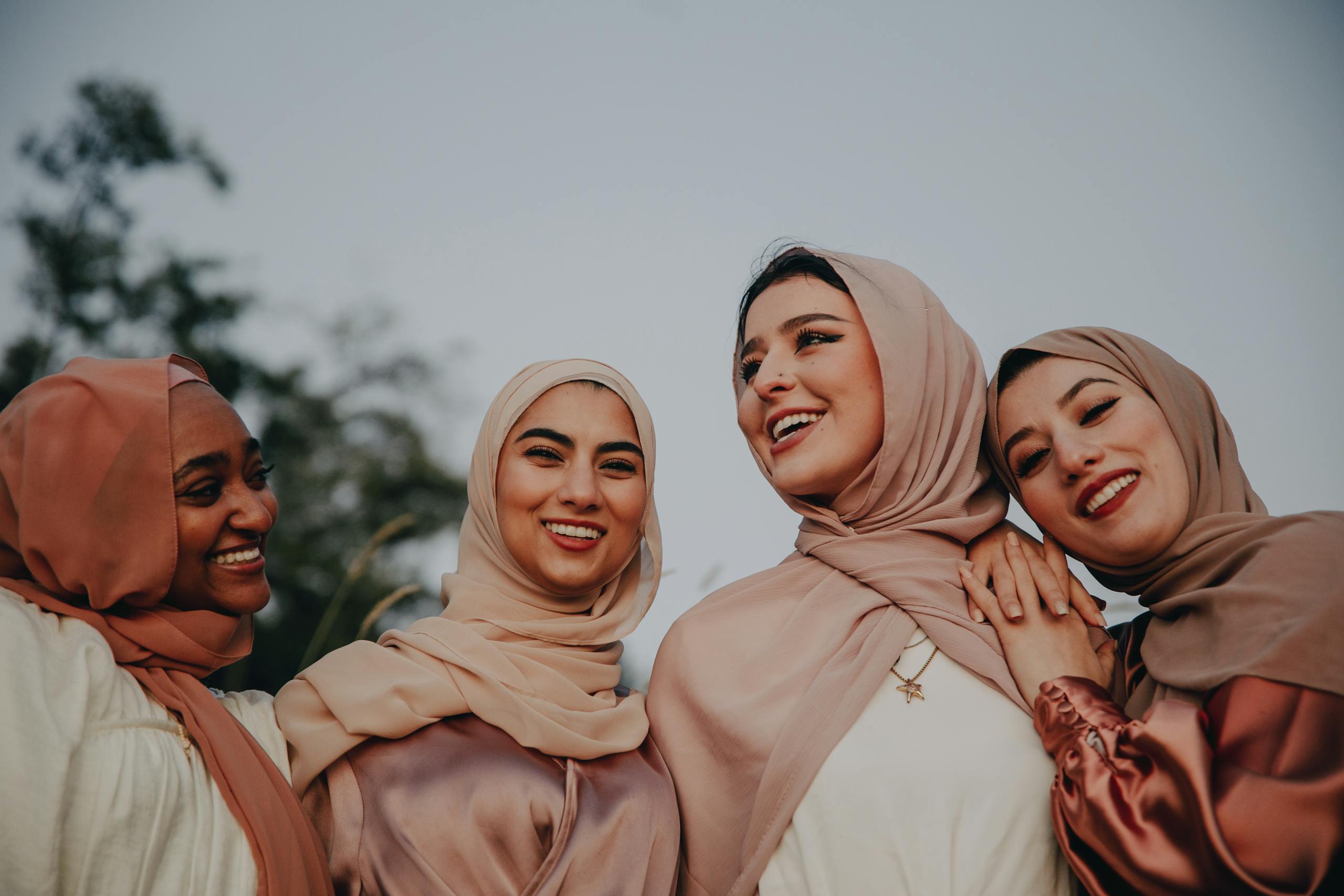 Four diverse women in hijabs laughing together outdoors, embracing friendship.