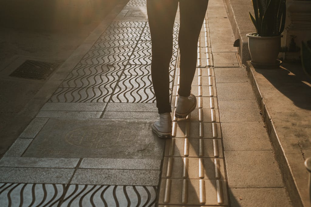 Silhouette of a person walking on a patterned street at sunset, highlighting urban fashion.